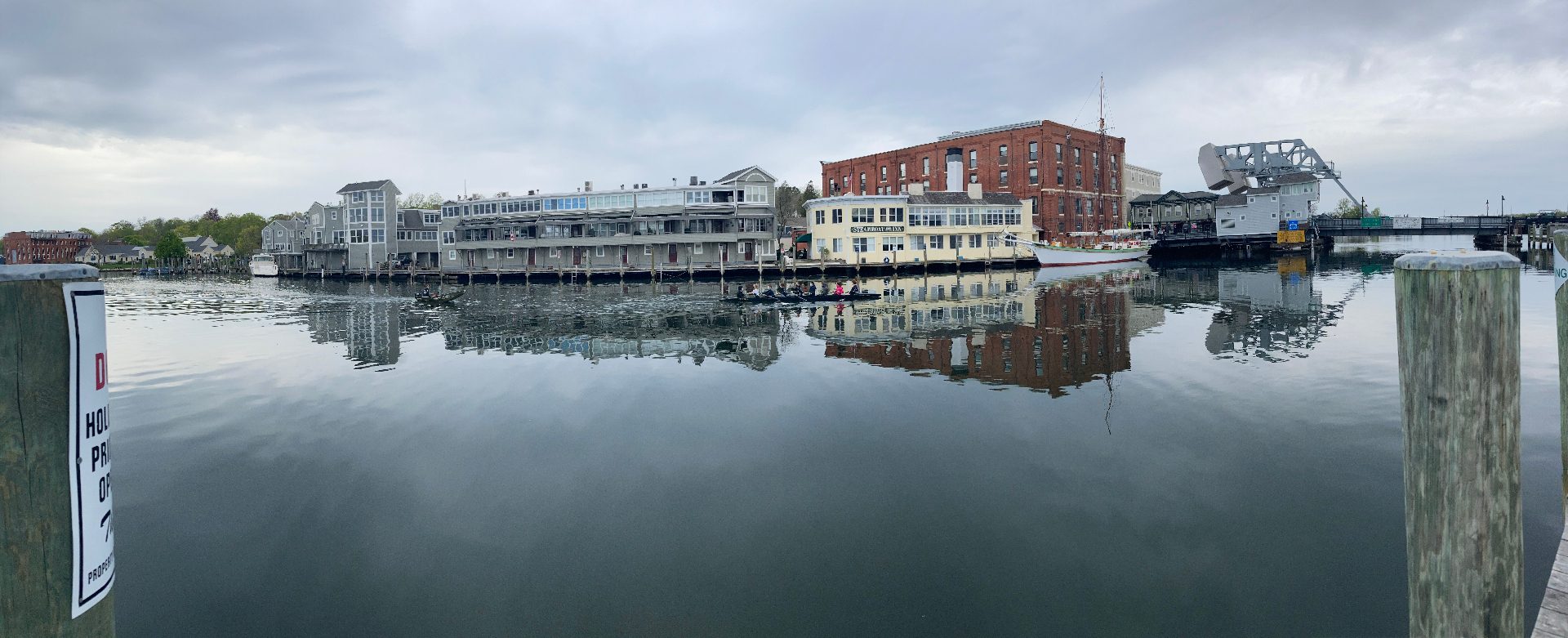 Panoramic view of the Mystic River boardwalk with glassy water reflecting the Steamboat Inn and the bascule bridge at rest