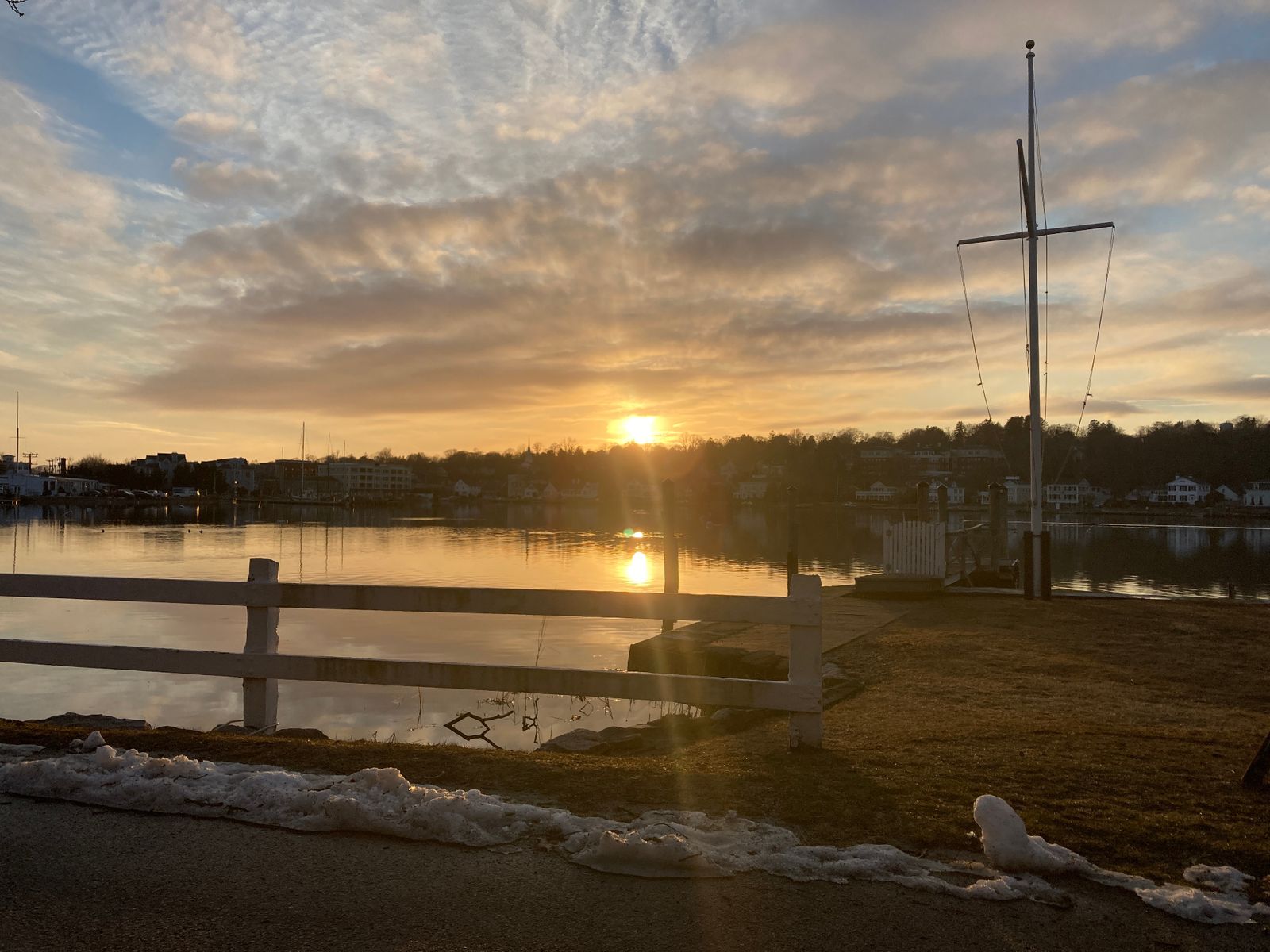 Golden hour sunset over Mystic harbor with sailboat mast silhouette